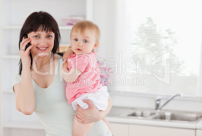 Beautiful woman on the phone while holding her baby in her arms