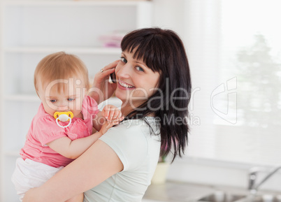 Good looking woman on the phone while holding her baby in her ar