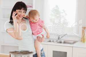 Attractive woman on the phone while holding her baby in her arms