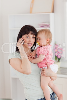 Lovely woman on the phone while holding her baby in her arms