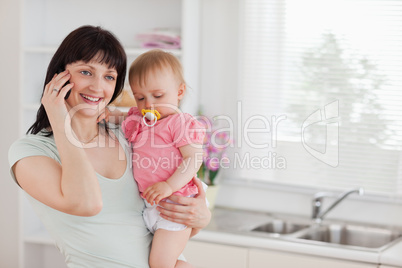 Pretty woman on the phone while holding her baby in her arms