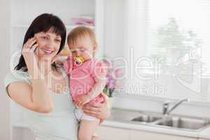 Pretty woman on the phone while holding her baby in her arms
