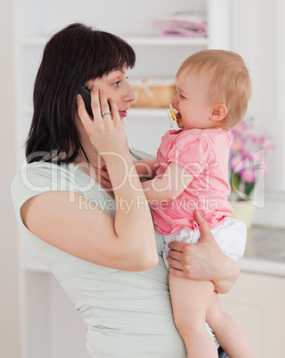 Lovely woman on the phone while holding her baby in her arms