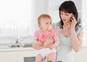 Lovely woman on the phone while holding her baby in her arms