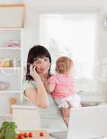 Beautiful brunette woman on the phone while holding her baby in