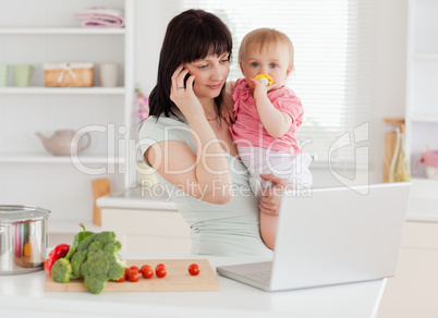 Good looking brunette woman on the phone while holding her baby