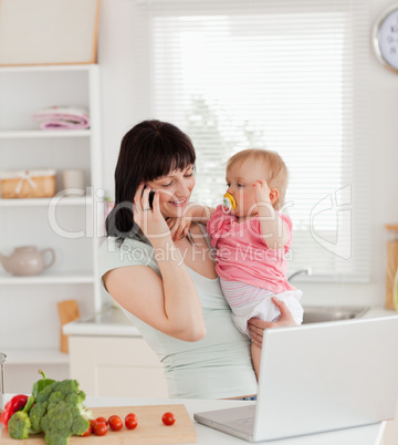 Attractive brunette woman on the phone while holding her baby in