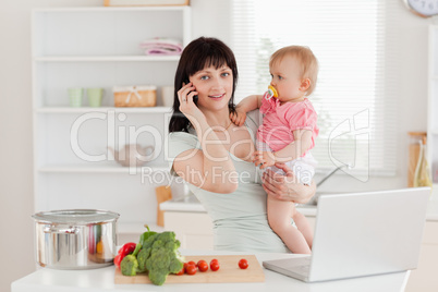 Charming brunette woman on the phone while holding her baby in h