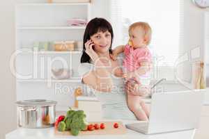 Charming brunette woman on the phone while holding her baby in h