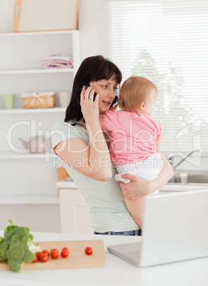 Pretty brunette woman on the phone while holding her baby in her