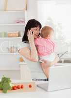 Pretty brunette woman on the phone while holding her baby in her
