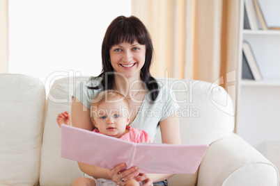 Good looking woman holding her baby and a book in her arms while