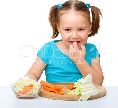 Little girl is cutting carrot for salad