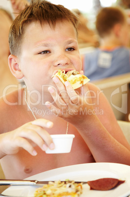 boy eats a pizza in summer cafe on a beach