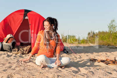 Camping happy woman sitting by campfire on beach