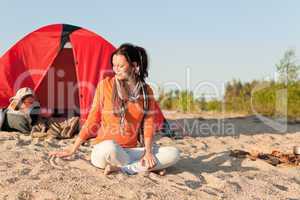 Camping happy woman sitting by campfire on beach