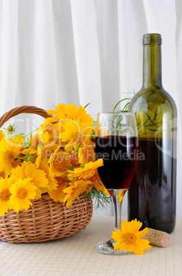 A bottle of rose wine with a glass and yellow flowers in a baske