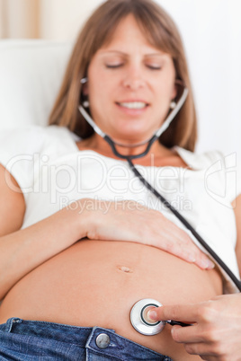 Facing view of a beautiful pregnant woman using a stethoscope wh