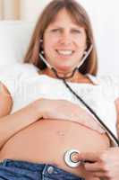 Facing view of an attractive pregnant woman using a stethoscope