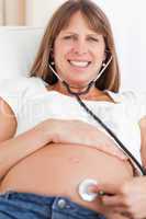 Facing view of a good looking pregnant woman using a stethoscope