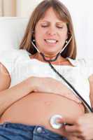 Facing view of a charming pregnant woman using a stethoscope whi