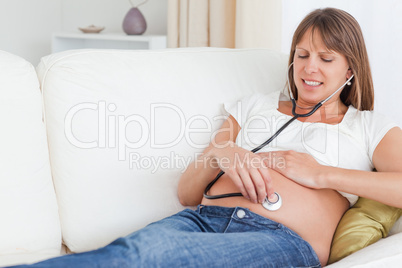 Attractive pregnant woman using a stethoscope while lying on a s