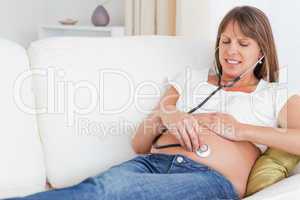 Attractive pregnant woman using a stethoscope while lying on a s