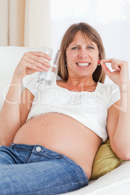 Beautiful pregnant woman taking a pill while lying on a sofa