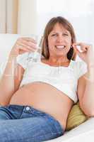 Beautiful pregnant woman taking a pill while lying on a sofa