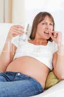 Good looking pregnant woman taking a pill while lying on a sofa