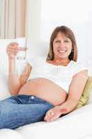 Pretty pregnant woman taking a pill while lying on a sofa