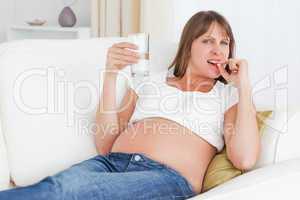 Charming pregnant woman taking a pill while lying on a sofa