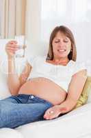 Attractive pregnant woman taking a pill while lying on a sofa
