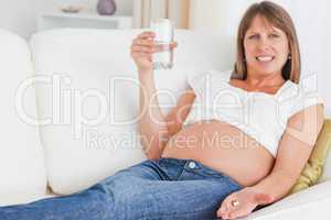 Cute pregnant woman taking a pill while lying on a sofa