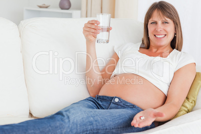 Gorgeous pregnant woman taking a pill while lying on a sofa