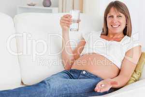 Gorgeous pregnant woman taking a pill while lying on a sofa