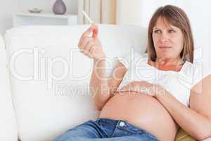 Attractive pregnant woman holding a cigarette while lying on a s