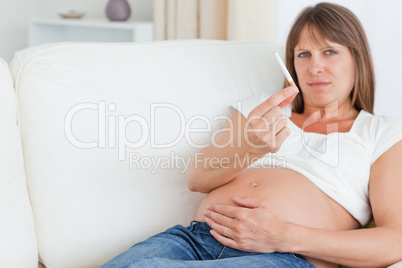 Charming pregnant woman holding a cigarette while lying on a sof