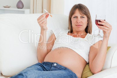Charming pregnant woman holding a cigarette and a glass of red w