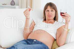 Charming pregnant woman holding a cigarette and a glass of red w