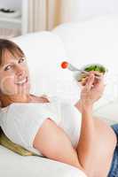Attractive pregnant woman eating a salad while lying on a sofa