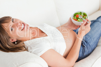 Lovely pregnant woman eating a salad while lying on a sofa