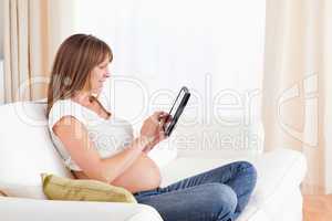 Lovely pregnant woman relaxing with a computer tablet while sitt