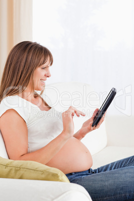 Attractive pregnant woman relaxing with a computer tablet while