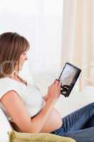 Good looking pregnant woman relaxing with a computer tablet whil
