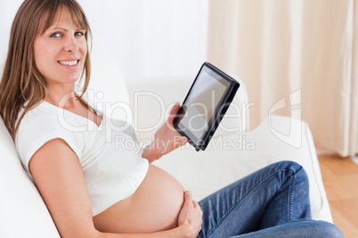 Charming pregnant woman relaxing with a computer tablet while si