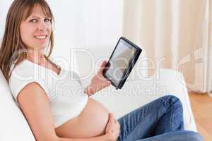 Charming pregnant woman relaxing with a computer tablet while si