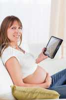 Pretty pregnant woman relaxing with a computer tablet while sitt