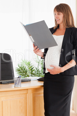 Charming pregnant female holding a file while standing