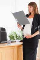 Charming pregnant female holding a file while standing